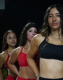 Three women in red and black tops posing against a dark background