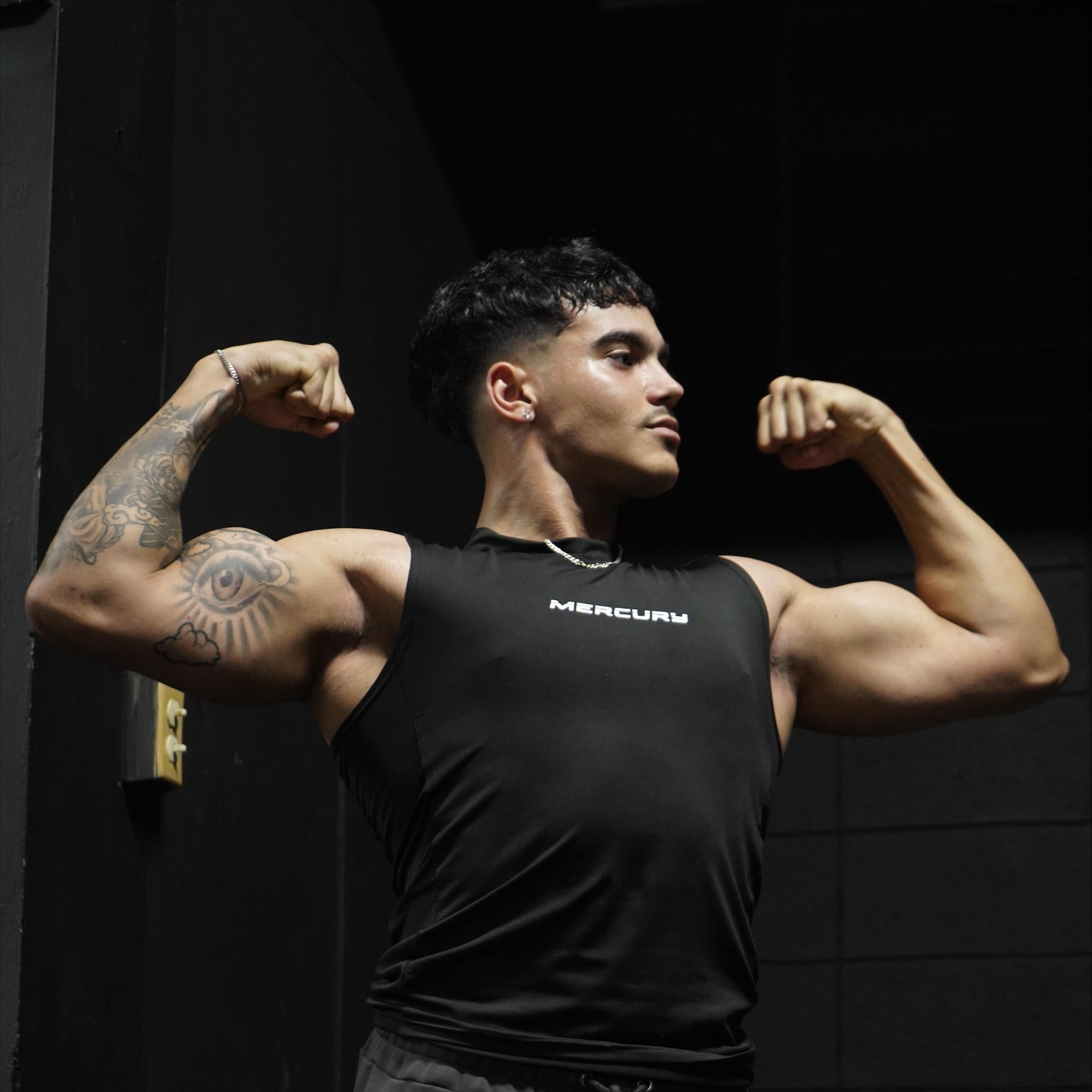 A person flexing their biceps while wearing black sweatpants and a black tank top.